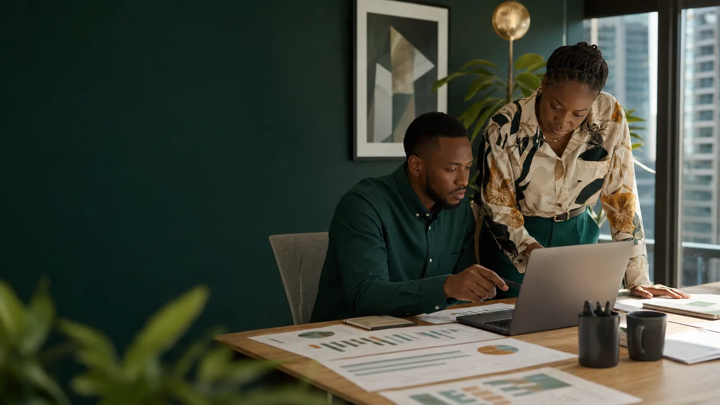 Two colleagues reviewing paid-media charts beside a laptop